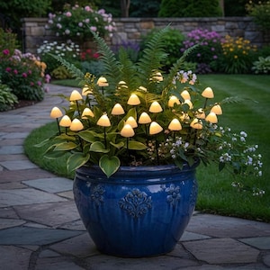 以下が含まれることがあります： 青い陶器の植木鉢に緑とキノコ型のライトが飾られています。ライトは温かい光を放ち、気まぐれな庭のシーンを作り出しています。植木鉢には花の模様があります。背景には石畳の小道と緑豊かな葉があります。