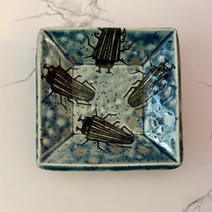 May include: A set of three ceramic mugs with a speckled, matte finish. The mugs are in shades of cream, light gray, and dark gray. Each mug has a simple, minimalist design, perfect for coffee or tea.