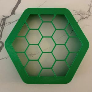 May include: A bright green, hexagonal object with a honeycomb pattern. The object is made of a solid material and has a series of hexagonal cutouts within its frame. The edges are smooth and rounded. The object is likely a decorative or functional item.