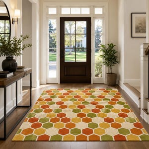 May include: A rectangular area rug featuring a repeating geometric honeycomb pattern in shades of orange, yellow, green, and cream. The rug is positioned on a wooden floor in a hallway, showcasing a consistent hexagonal tile-like design throughout.