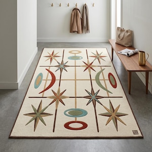 May include: A rectangular cream-colored rug with a geometric design featuring starbursts, circles, and crescent shapes in shades of brown, red, blue, and green. The rug has a dark brown border and is placed in a hallway.