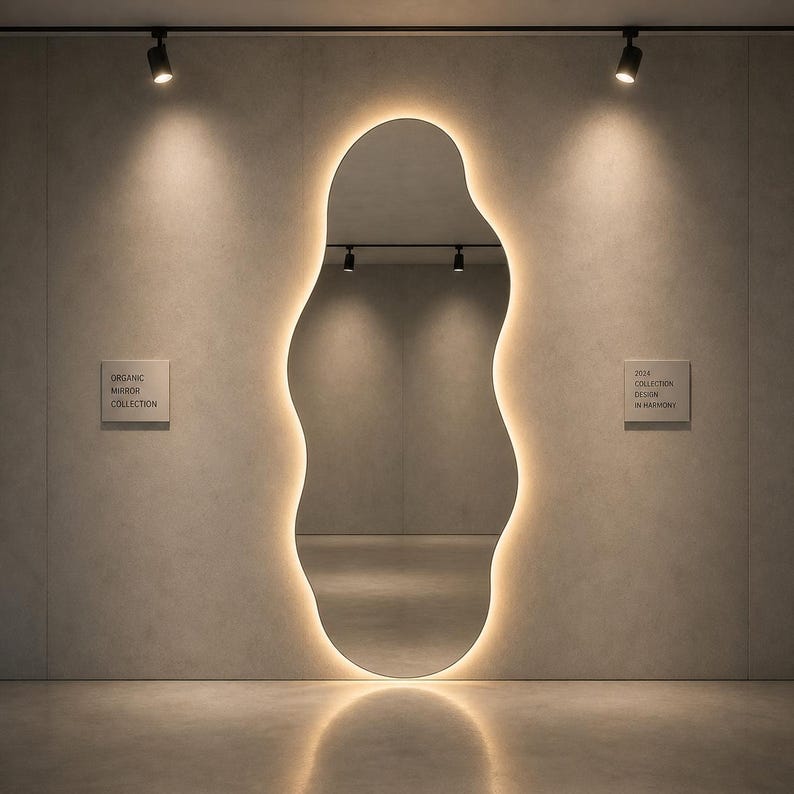 May include: An organically shaped mirror with a warm, glowing light outlining its form. The mirror is mounted on a neutral-toned wall, with the text "ORGANIC MIRROR COLLECTION" and "2024 COLLECTION DESIGN IN HARMONY" displayed on small plaques.