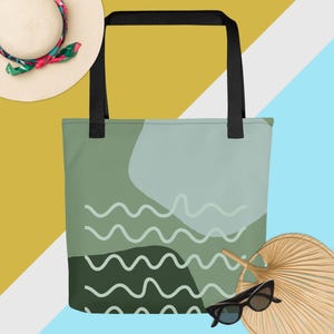 Peut inclure: Un sac fourre-tout vert avec un motif ondulé blanc. Le sac a des poignées noires et est à côté d'un chapeau de paille avec un foulard floral, des lunettes de soleil et un éventail.