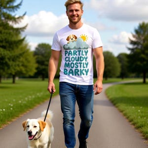 Może przedstawiać: Biały t-shirt z krótkim rękawem z grafiką szczeniaka wyglądającego zza szarej chmury obok żółtego słońca. Tekst nadrukowany turkusowymi literami brzmi "PARTLY CLOUDY, MOSTLY BARKY" w ułożeniu pionowym na przedniej części odzieży.