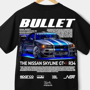 Puede incluir: Camiseta negra con un diseño gráfico de un Nissan Skyline GT-R R34, con detalles en azul y blanco. La camiseta incluye la palabra "BULLET" y texto sobre las especificaciones e historia del coche. También se ven los logotipos de Sparco, HKS, JBL y Nopi.