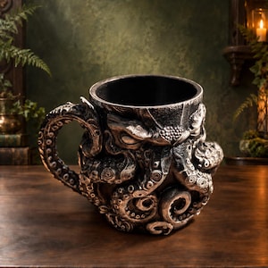 May include: A dark gray and black mug featuring a three-dimensional sculpted octopus design. The handle is shaped like a curved tentacle, and the exterior surface is covered in detailed suckers and textured skin patterns wrapping around the vessel.