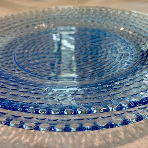 May include: A stack of three light blue glass plates. Each plate has a textured, dotted pattern across the surface and a slightly raised rim. The plates are transparent, allowing light to pass through, and are stacked on top of each other.