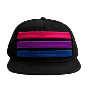 Peut inclure: Casquette de baseball noire avec une visière plate. Elle présente trois bandes horizontales roses, violettes et bleues, représentant le drapeau de la fierté bisexuelle. Les rayures sont en matière texturée.
