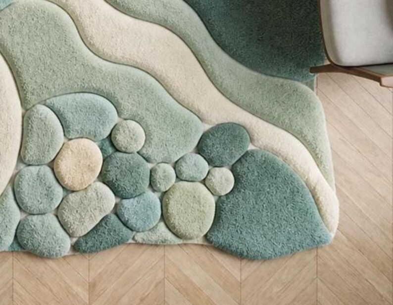 May include: A textured area rug with a pebble and wave design. The rug features light green, beige, and teal colours. The rug's design includes rounded shapes resembling stones and flowing wave patterns.