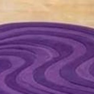 May include: A wavy, purple rug with a textured surface. The rug's design features a series of curved lines, creating a flowing, organic pattern. The rug is placed on a light-colored wooden floor.