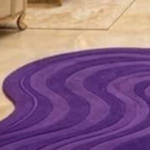 May include: A purple, wavy-patterned rug with varying shades of violet and lavender. The rug's design features flowing, curved lines, creating a dynamic and textured appearance. The rug is placed on a light-colored floor.