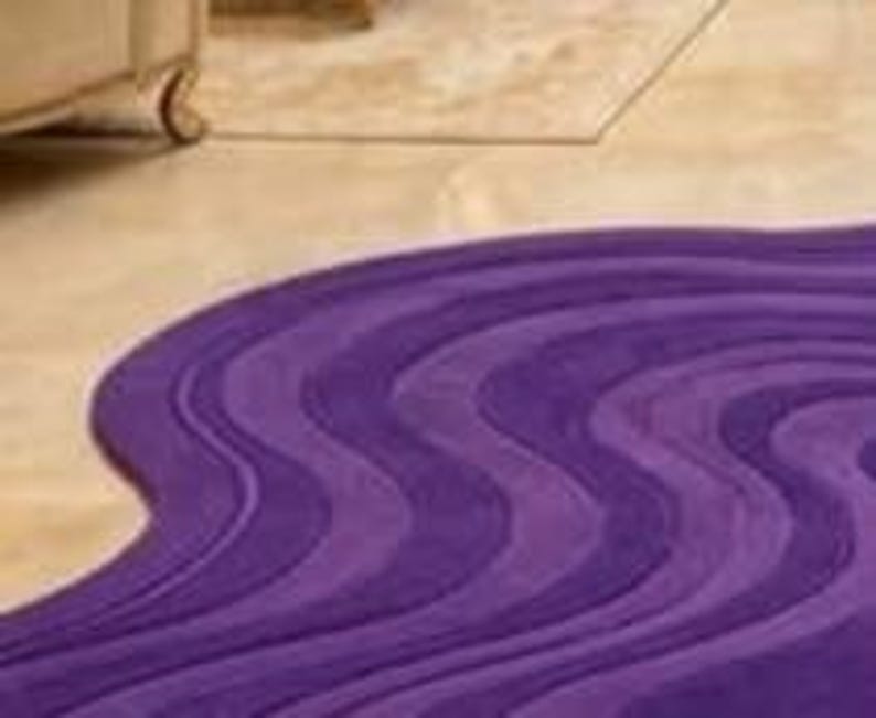 May include: A purple, wavy-patterned rug with varying shades of violet and lavender. The rug's design features flowing, curved lines, creating a dynamic and textured appearance. The rug is placed on a light-colored floor.