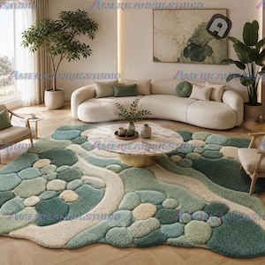 May include: An abstract area rug with a pebble design in shades of green, beige, and cream. The rug is in a living room with a curved sofa, armchairs, and a round coffee table. The room has large windows and a neutral colour palette.