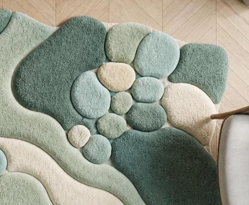 May include: A textured rug in shades of green, blue, and cream, with a design reminiscent of pebbles and flowing forms. The rug's pattern creates a natural, organic look. This decorative floor covering would suit a living room or bedroom.