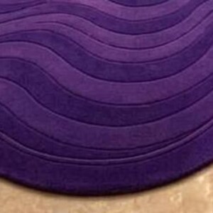 May include: A plush, purple area rug with a wave-like design. The rug features a series of curved lines, creating a textured, three-dimensional effect. The deep purple color adds a touch of elegance and sophistication to any room.