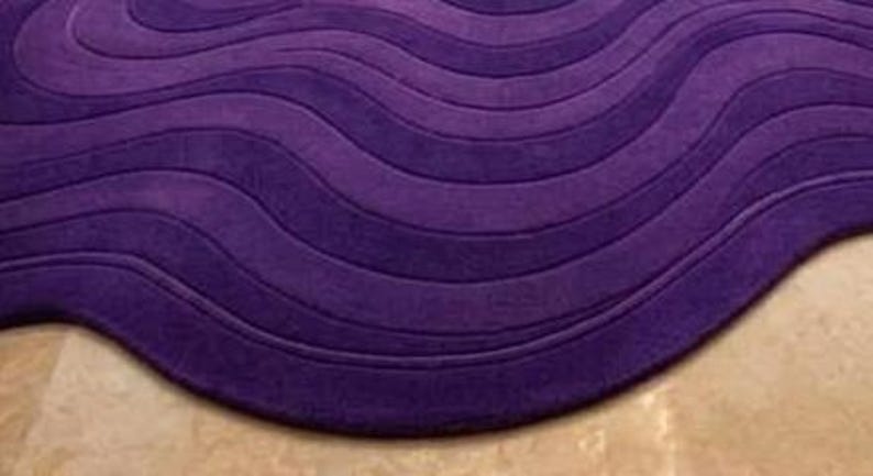 May include: A plush, purple area rug with a wave-like design. The rug features a series of curved lines, creating a textured, three-dimensional effect. The deep purple color adds a touch of elegance and sophistication to any room.