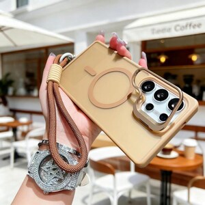 May include: A tan phone case with a ring holder and a matching lanyard. The case has a circular design on the back and a gold-colored ring holder. The lanyard is brown and tan.