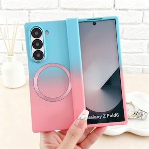 May include: A bi-color phone case for a Samsung Galaxy Z Fold6. The case transitions from blue to pink, featuring a camera array and a circular design. The phone screen is visible, and the case is held open.