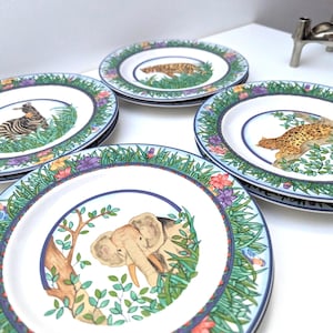 Op de afbeelding: Een set witte keramische borden met een junglethema. Elk bord toont een ander dier: een zebra, een luipaard en een olifant. De borden hebben een blauwe rand en zijn versierd met kleurrijke bloemen en bladeren.