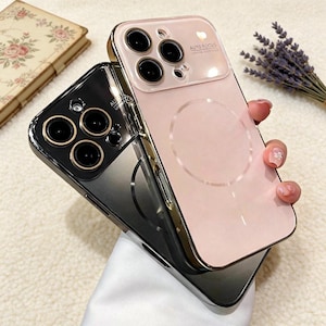 May include: Two phone cases, one black and one pink, are stacked. The pink case has a gold-colored frame and the words "AUTO FOCUS" printed on it. The black case has a gold-colored frame. Both cases have a circular design on the back.