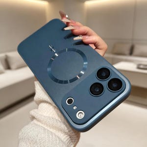 Op de afbeelding: Een teal telefoonhoesje met een cirkelvormige magnetische bevestiging en een cameramodule met drie lenzen. De hoes heeft een gladde afwerking en een opstaande rand rond de camera. De telefoonhoes is ontworpen om de telefoon te beschermen.