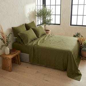 May include: A bed set featuring olive green bedding, including a flat sheet, a fitted sheet, and four matching pillowcases. The fabric has a visible textured weave. The bed is neatly made with the olive green linens covering the mattress and pillows.