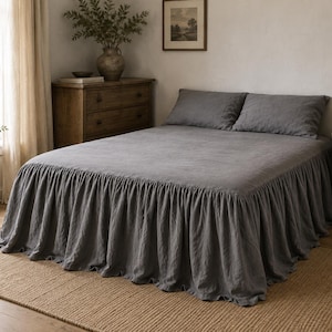 May include: A charcoal gray bedspread featuring a long, gathered ruffle skirt that extends to the floor. The set includes two matching rectangular pillow shams in the same dark gray fabric, creating a uniform look across the entire bed surface.