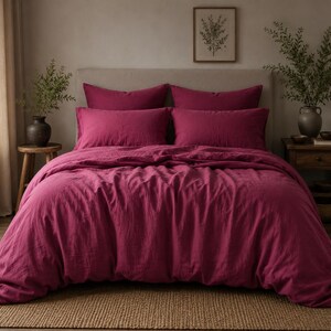 Può includere: Un set di biancheria da letto color magenta intenso composto da un copripiumino e quattro federe rettangolari abbinate. Il tessuto presenta una trama visibile e strutturata, drappeggiato su un letto con testiera di colore neutro.