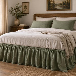 May include: A bed featuring a sage green ruffled bed skirt, a light beige duvet cover, and two matching sage green rectangular throw pillows. The bed is set against a wooden headboard, with a neutral-toned throw blanket draped over the foot.