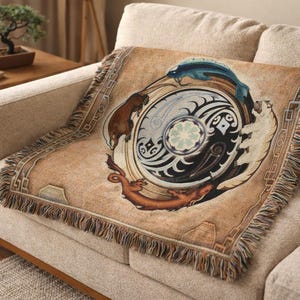 Op de afbeelding: Een beige sprei met een gedetailleerd cirkelvormig ontwerp met dieren en een centraal yin-yang-symbool. De deken heeft een gefranjerde rand en is gedrapeerd over een beige bank, wat een gezellige uitstraling creëert.