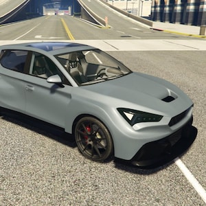 Peut inclure: Une voiture grise à hayon avec des roues noires et des étriers de frein rouges. La voiture a un toit ouvrant et est garée sur une surface pavée. Les phares sont noirs et angulaires.