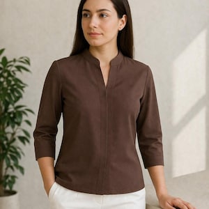 Peut inclure: Une femme porte un chemisier marron à manches trois-quarts avec un col officier et une encolure en V. Le chemisier est associé à un pantalon blanc. Le texte "sytarto STYLE WITH CONFIDENCE" est en haut de l'image.
