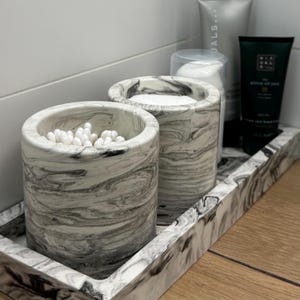 Puede incluir: Un juego de tres tazas de cerámica con acabado moteado y mate. Las tazas son de color crema, gris claro y gris oscuro. Cada taza tiene un diseño simple y minimalista.
