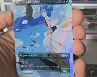 以下が含まれることがあります： Birds of Paradiseと題されたホログラフィック仕様のトレーディングカード。青い髪で白い服を着たアニメスタイルのキャラクターが、雲や鳥の間を飛んでいる様子が描かれています。カードにはCreature - Bird、Flying、Add one mana of any colorと記載されています。