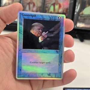 May include: A holographic "Counterspell" trading card featuring an image of a person making a rude gesture. The card has a blue border and the text "Counter target spell."