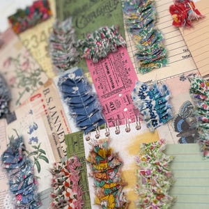 May include: A collection of fabric ruffles in various floral and solid patterns, featuring frayed edges and visible stitching, arranged over a background of vintage-style ephemera, including ledger paper, tickets, and botanical illustrations.