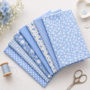 May include: A stack of seven folded fabric squares in various shades of light blue and white. Patterns include white polka dots on blue, blue and white gingham, blue floral prints, and blue and white stripes. Includes a spool of blue thread and scissors.