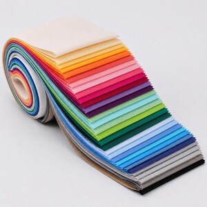 May include: A roll of fabric strips featuring a spectrum of colors including cream, yellow, orange, pink, purple, green, blue, gray, and black. The fabric is tightly coiled at one end and fans out into individual layers of varying hues.