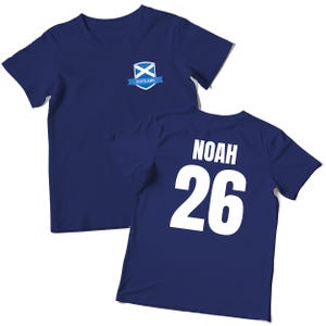 Puede incluir: Camiseta azul marino con el nombre "NOAH" y el n&uacute;mero "26" impresos en blanco en la espalda. La parte delantera presenta un escudo de la bandera escocesa con la palabra "SCOTLAND" en una cinta azul.
