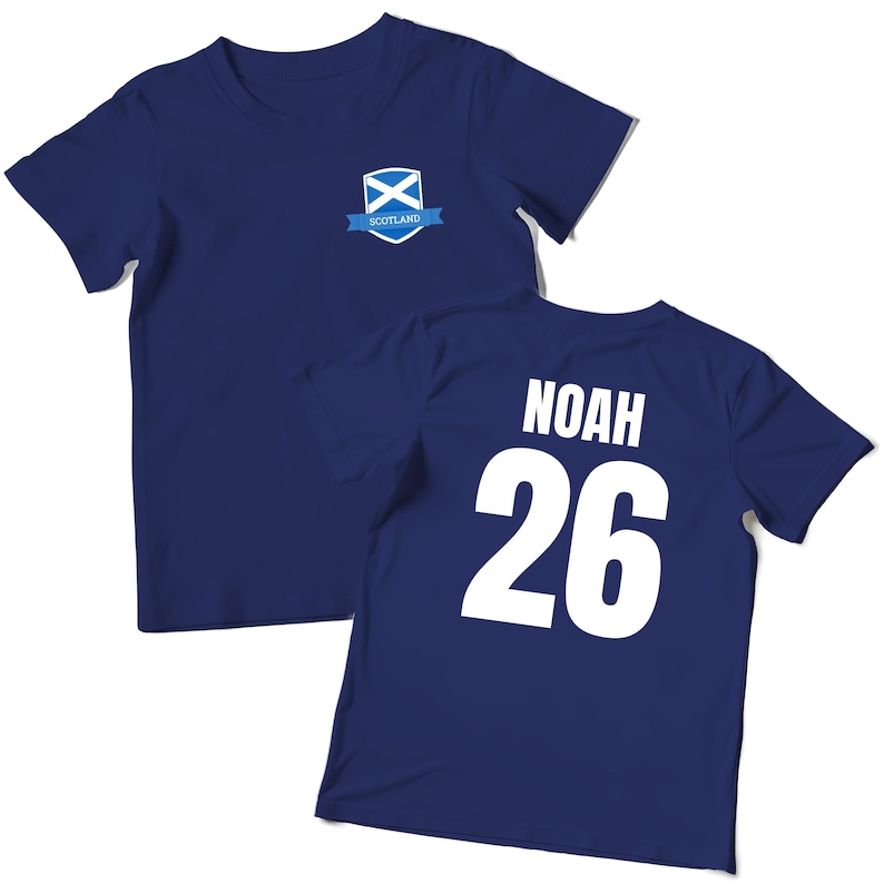 Puede incluir: Camiseta azul marino con el nombre "NOAH" y el n&uacute;mero "26" impresos en blanco en la espalda. La parte delantera presenta un escudo de la bandera escocesa con la palabra "SCOTLAND" en una cinta azul.