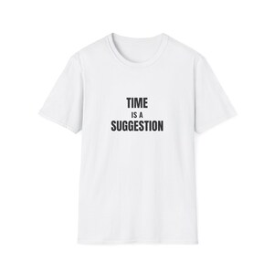 Puede incluir: Camiseta blanca con el texto negro "TIME IS A SUGGESTION". La camiseta tiene cuello redondo y mangas cortas. El texto está centrado en la parte delantera de la prenda.