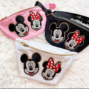 Puede incluir: Tres ri&ntilde;oneras rosas, negras y blancas, cada una con apliques de Mickey y Minnie Mouse. La ri&ntilde;onera rosa tiene una correa negra, la negra tiene una correa negra y la blanca tiene una cremallera dorada.