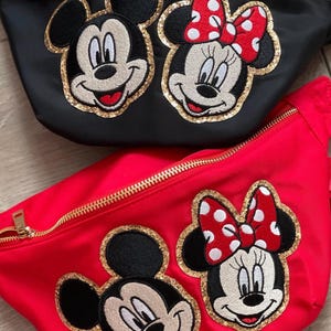 Puede incluir: Dos ri&ntilde;oneras, una negra y otra roja, con cremalleras doradas. Cada ri&ntilde;onera presenta bordados de las caras de Mickey y Minnie Mouse con detalles de purpurina dorada. Minnie tiene un lazo rojo con lunares blancos.