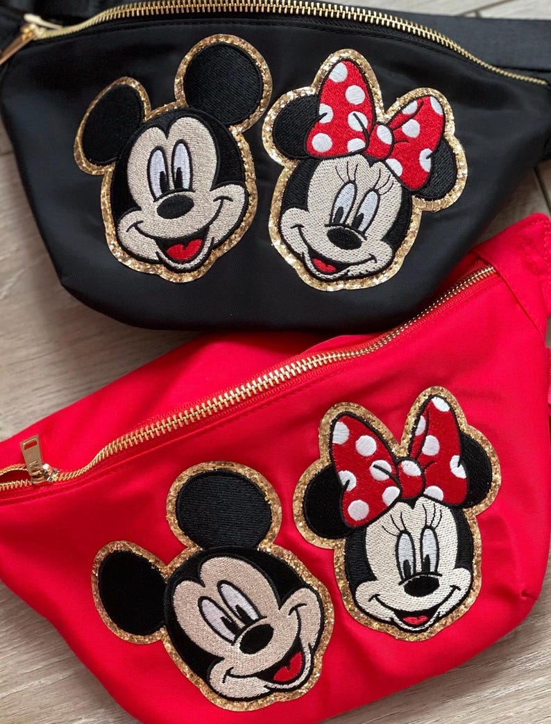 Puede incluir: Dos ri&ntilde;oneras, una negra y otra roja, con cremalleras doradas. Cada ri&ntilde;onera presenta bordados de las caras de Mickey y Minnie Mouse con detalles de purpurina dorada. Minnie tiene un lazo rojo con lunares blancos.