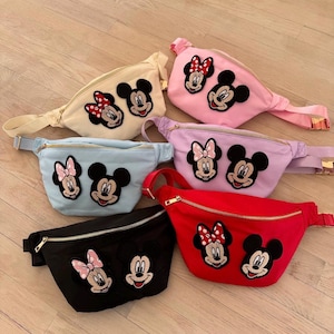 Puede incluir: Seis ri&ntilde;oneras de colores, cada una con cierre de cremallera y correa ajustable. Las ri&ntilde;oneras son de color negro, rojo, rosa, azul claro, lavanda y crema. Cada una tiene un dise&ntilde;o bordado de Mickey y Minnie Mouse.