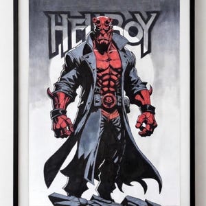 May include: Framed artwork depicting a red-skinned character with horns, wearing a black coat and belt with a skull buckle. The word "HELLBOY" is displayed above the character in a stylized font. The artwork is in black, white, and red.