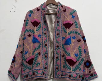 May include: A mauve jacket featuring intricate floral embroidery in shades of dark red, bright blue, and green. The garment has a stand-up collar, long sleeves, and an open front that reveals a black and white vertical striped lining inside.
