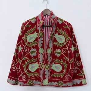 May include: A deep red velvet jacket featuring intricate embroidery in shades of light green, olive, and grey. The design showcases floral and leaf motifs across the front panels and sleeves, with a vertical striped lining visible at the collar.