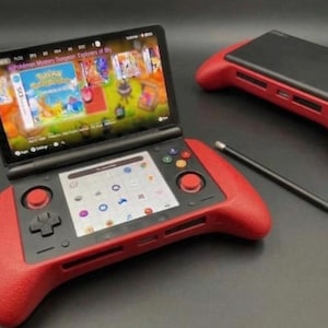 Könnte beinhalten: Ein tragbares Spielgerät mit rotem Griff und schwarzem Bildschirm, auf dem eine Spieloberfläche angezeigt wird. Das Gerät hat Tasten und einen Joystick. Ein Stift und ein zweites Gerät sind ebenfalls sichtbar.