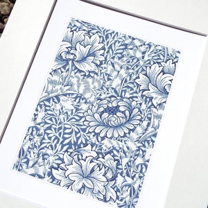 May include: A framed print featuring a blue and white floral pattern. The artwork showcases a detailed design of stylized flowers and foliage against a white background. The print is matted and framed in white, creating a clean and classic presentation.